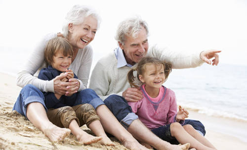 starí rodičia sedia so svojimi vnúčatami na pláži a smejú sa