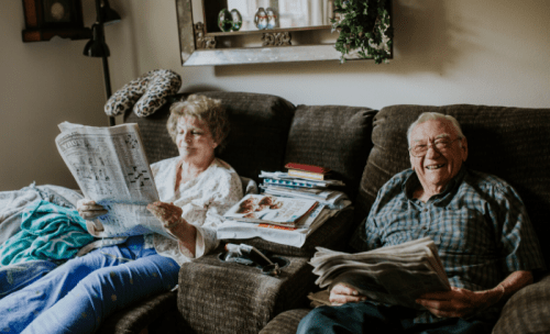 starší pár sedí na gauči a číta noviny